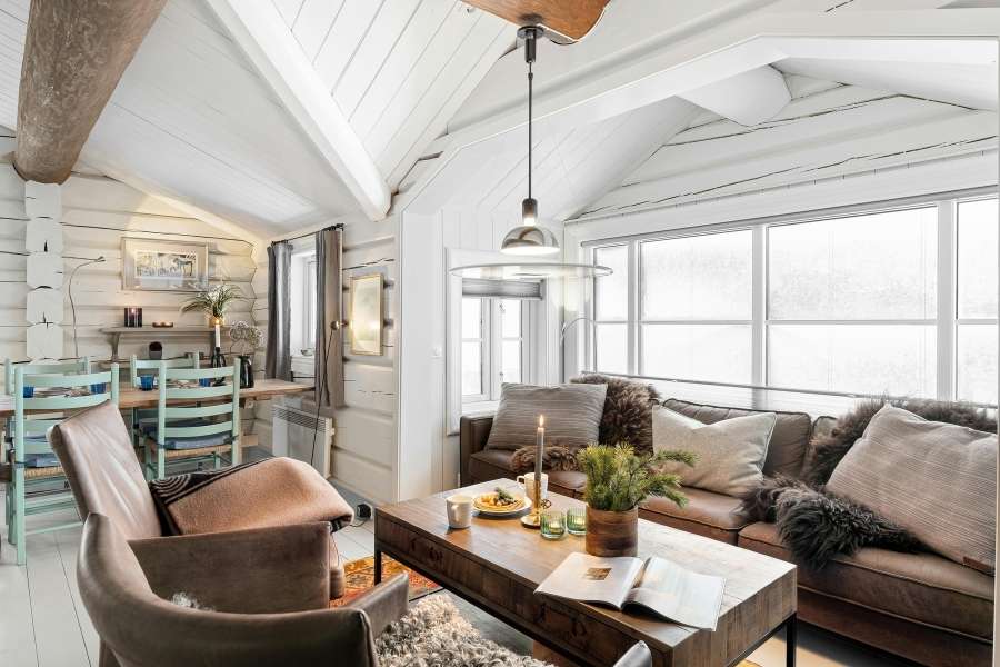 Coin lecture chaleureux dans un chalet avec fauteuil en cuir, canapé moelleux et charpente bois blanche