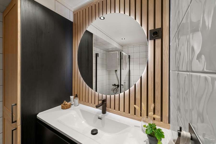 Mur d'accent en lattes de bois clair derrière un miroir rond dans une salle de bain moderne.